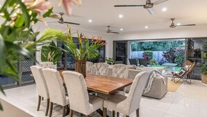 A modern dining area with a wooden table and chairs, ceiling fans, and large windows offering a view of the outdoors. - Luxury Tropical Escape: Beachside Villa with Heated Pool & Modern Comforts (Trinity Beach)