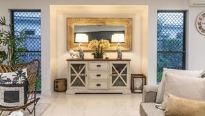A living room with a white sofa, a wooden cabinet with glass doors, a large mirror, and a potted plant. - Luxury Tropical Escape: Beachside Villa with Heated Pool & Modern Comforts (Trinity Beach)