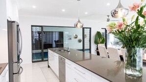 A modern kitchen with a central island, stainless steel appliances, and a glass door leading to a balcony. - Luxury Tropical Escape: Beachside Villa with Heated Pool & Modern Comforts (Trinity Beach)