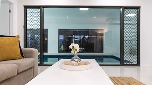 A modern living room with a sofa, a white coffee table, and a view through large glass doors. - Luxury Tropical Escape: Beachside Villa with Heated Pool & Modern Comforts (Trinity Beach)
