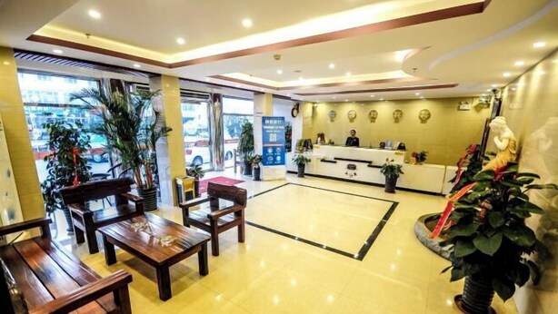 Un hall de hotel con mostrador de recepción, zona de estar y plantas en macetas.