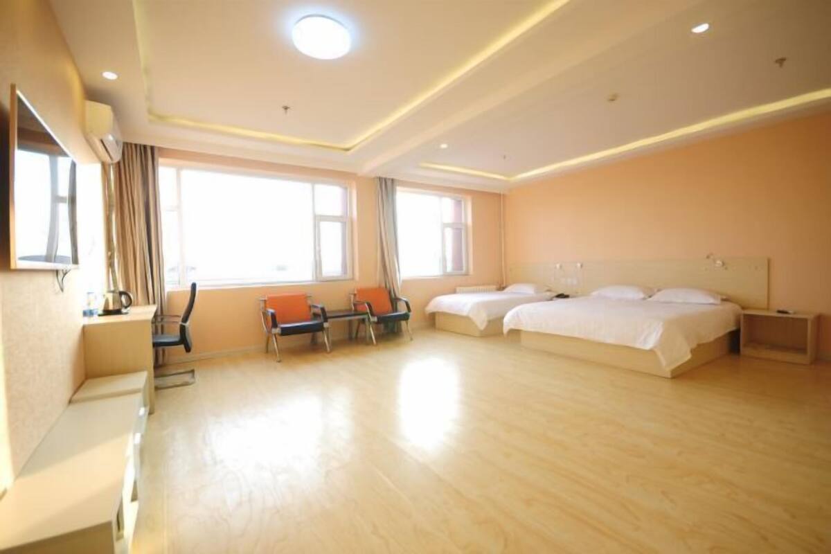 A hotel room with a large bed, two smaller beds, a desk with a chair, and a sofa.