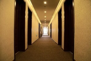 A long, narrow hotel corridor with doors on both sides, leading to a bright room at the end. - Richmond Holiday Hotel (Qinhuangdao Shanhaiguan Laolongtou Resort) (Qinhuangdao)