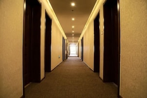 Un largo y estrecho pasillo de hotel con puertas a ambos lados, que conduce a una habitación luminosa al final.