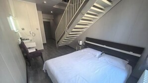 Una habitación de hotel moderna con una cama grande, un escritorio con silla, una mesita y una escalera.