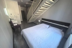 Camera d'albergo moderna con un letto grande, una scrivania con sedia, un tavolino e una scala.