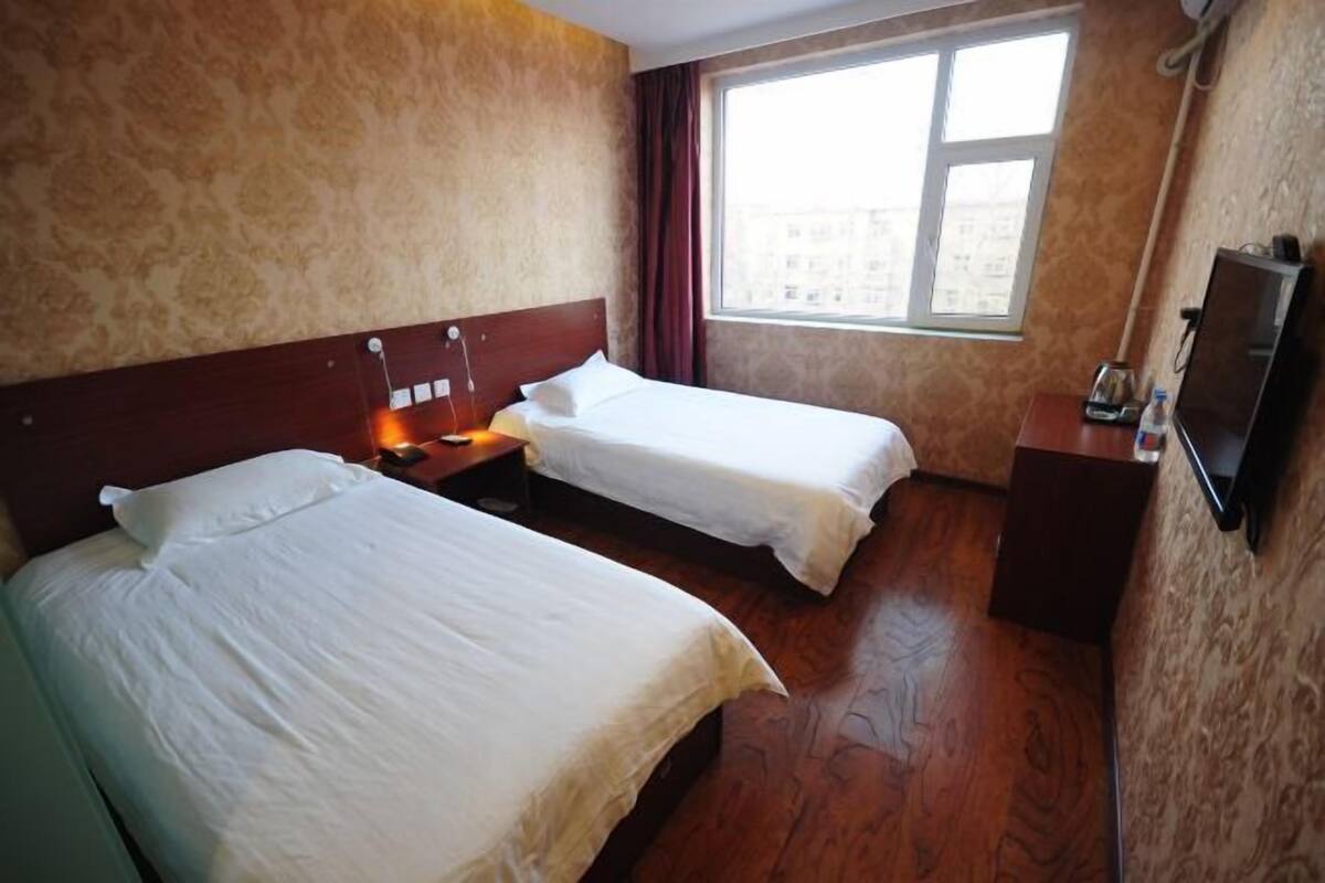 A hotel room with two beds, a TV, a window, and a wooden floor.