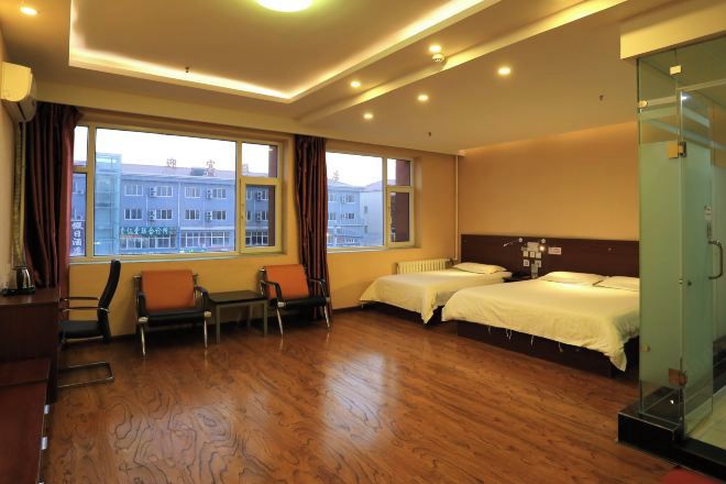 A hotel room with two beds, a seating area with chairs, a large window with a view of buildings, and a glass partition.