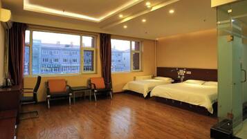A hotel room with two beds, a seating area with chairs, a large window with a view of buildings, and a glass partition.