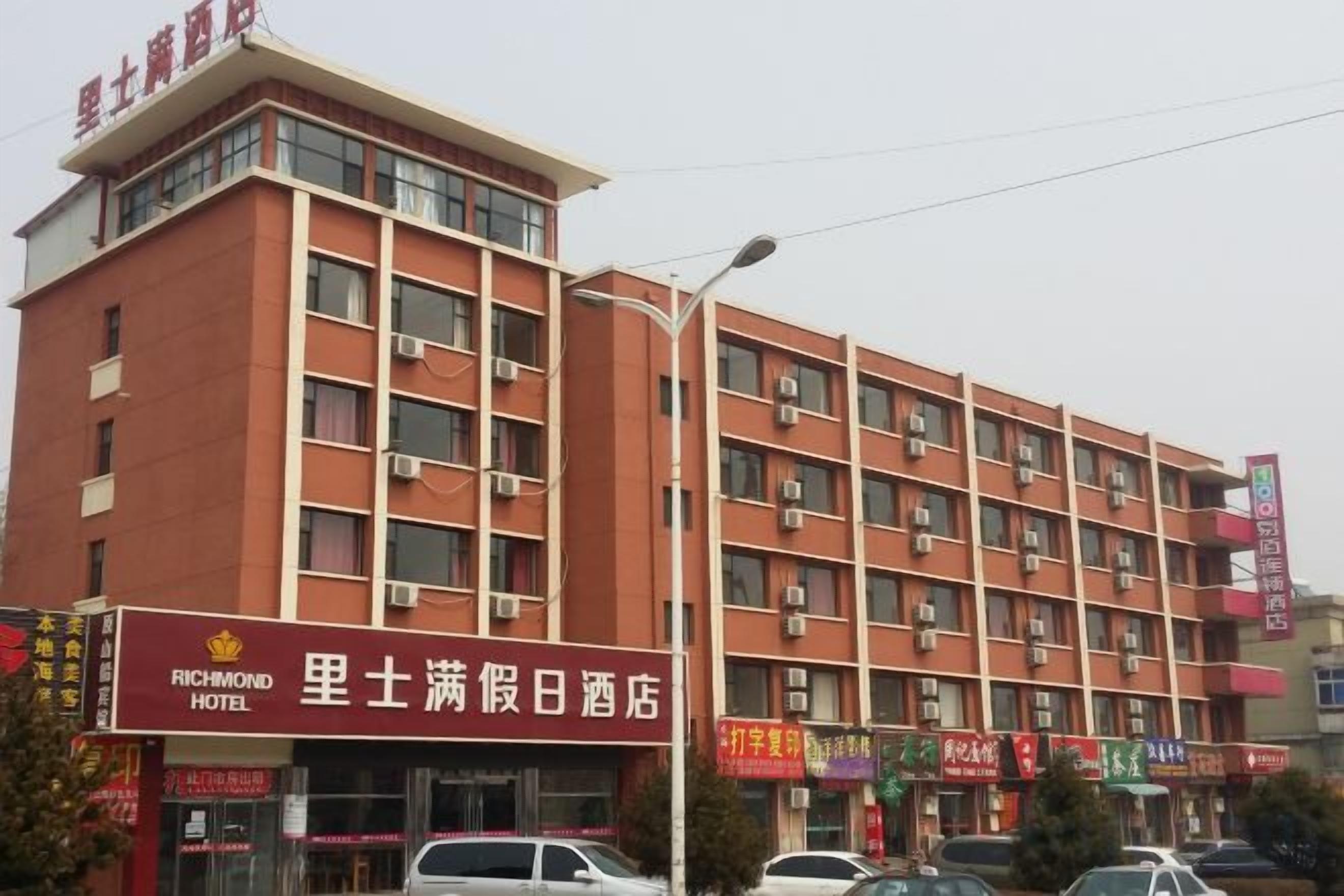 Ein mehrstöckiges Hotel mit roter Fassade, mehreren Balkonen und verschiedenen Geschäften im Erdgeschoss.