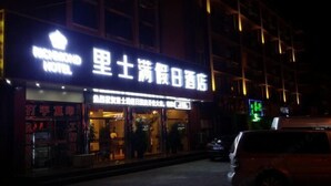 Un hotel con un cartel en un idioma extranjero, entrada visible y un coche estacionado afuera.
