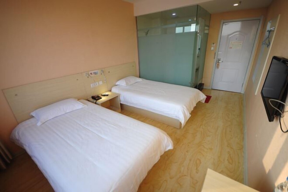 Habitación de hotel con dos camas, televisión y cabina de ducha de vidrio.