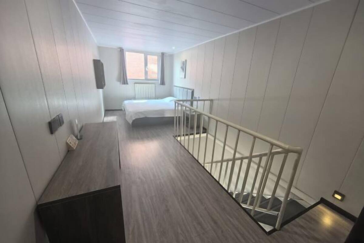 A modern hotel room with a wooden floor, a bed, a desk, and a white railing.