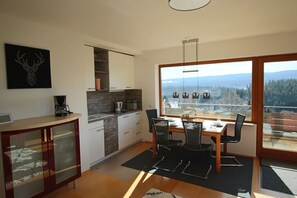 A modern kitchen with a dining area, large windows with a view of mountains, and a fireplace. - App. in Haus Feldbergblick with pool, sauna and fitness in Lenzkirch (Lenzkirch)