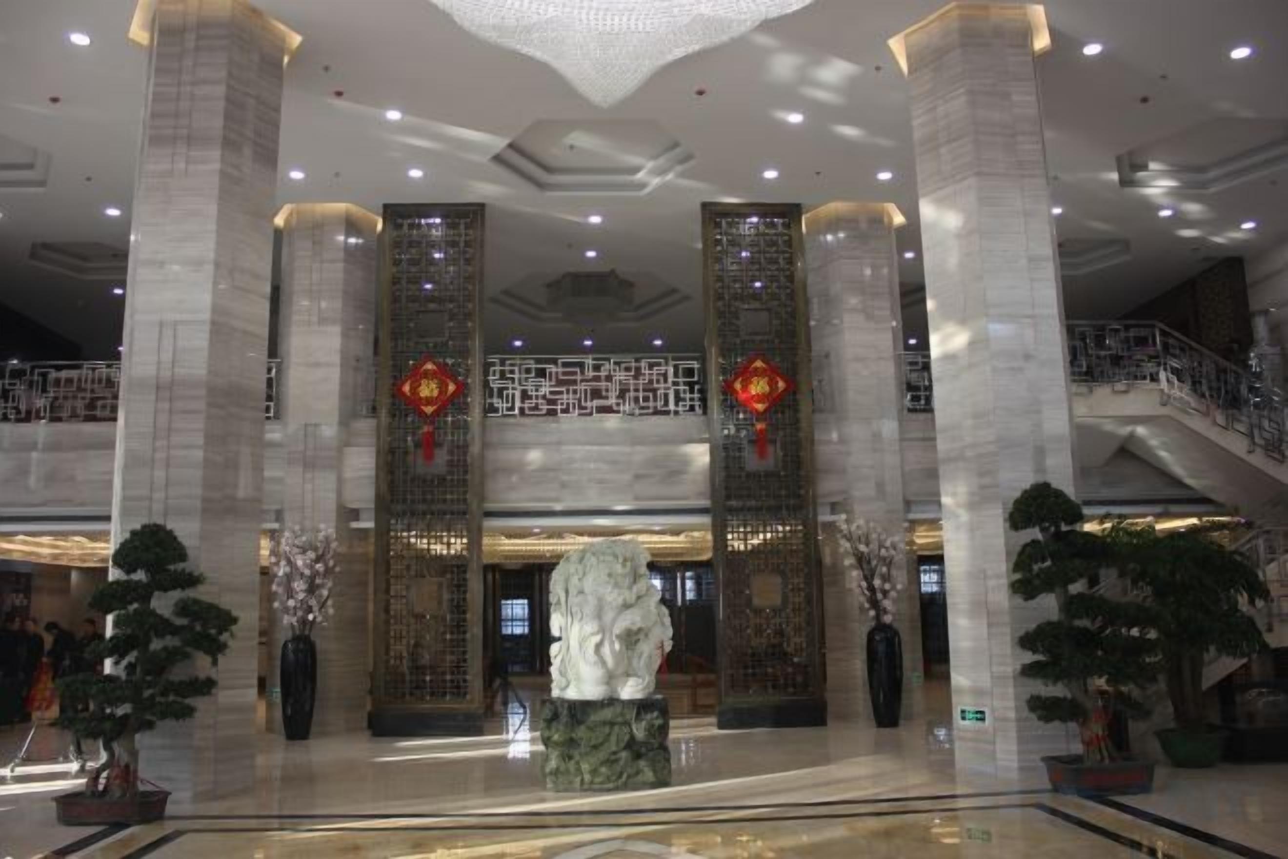 A lobby with marble columns, a central sculpture, and a staircase leading to an upper level.