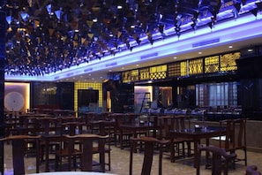 A spacious restaurant with multiple dining tables and chairs, a patterned wall design, and a ceiling with hanging lights. - Chiping Hotel (Liaocheng)