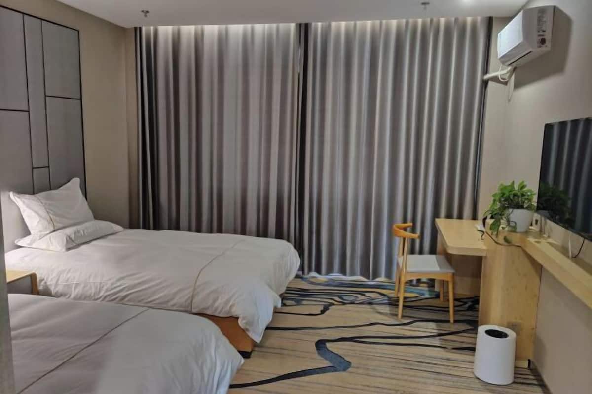 A hotel room with two beds, a desk, a chair, a TV, and a plant.