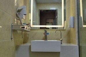 Un baño con lavamanos blanco, un espejo, dispensador de toallas y cabina de ducha de vidrio.