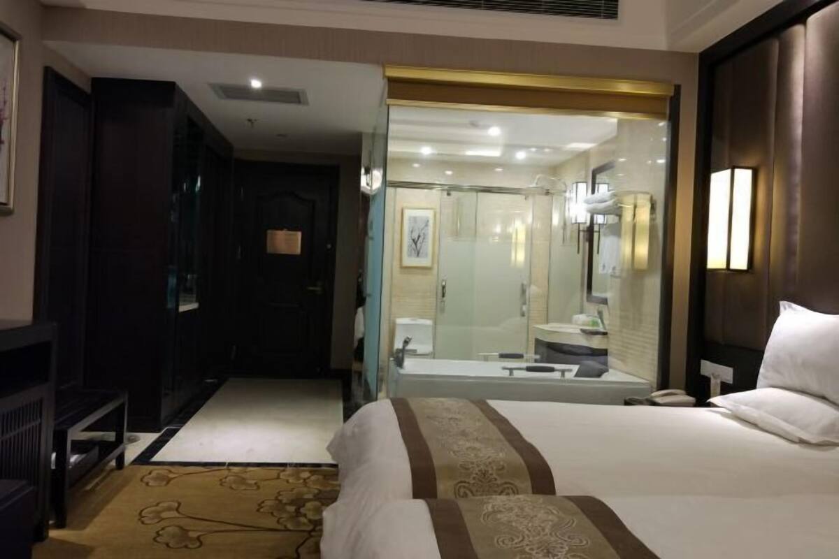 A hotel room with a large bed, a bathroom with a glass shower enclosure, and a desk with a chair.