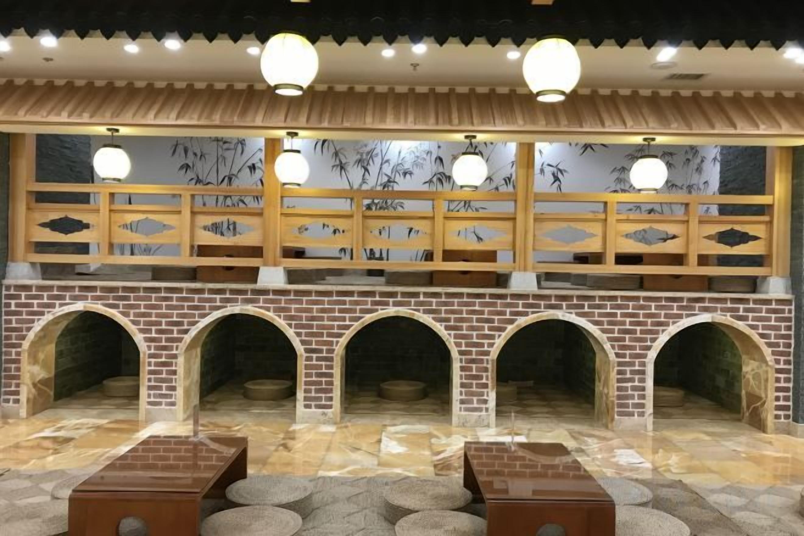 Habitación de estilo tradicional con suelo de baldosas, paredes de ladrillo y techo de madera. Se observan cuatro nichos de arco y un área de estar central con una mesa y sillas.