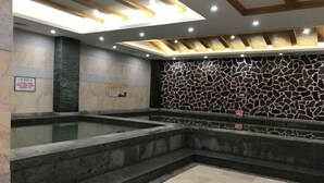 A spa area with two hot tubs, a stone wall, and a tiled floor. - Chiping Hotel (Liaocheng)