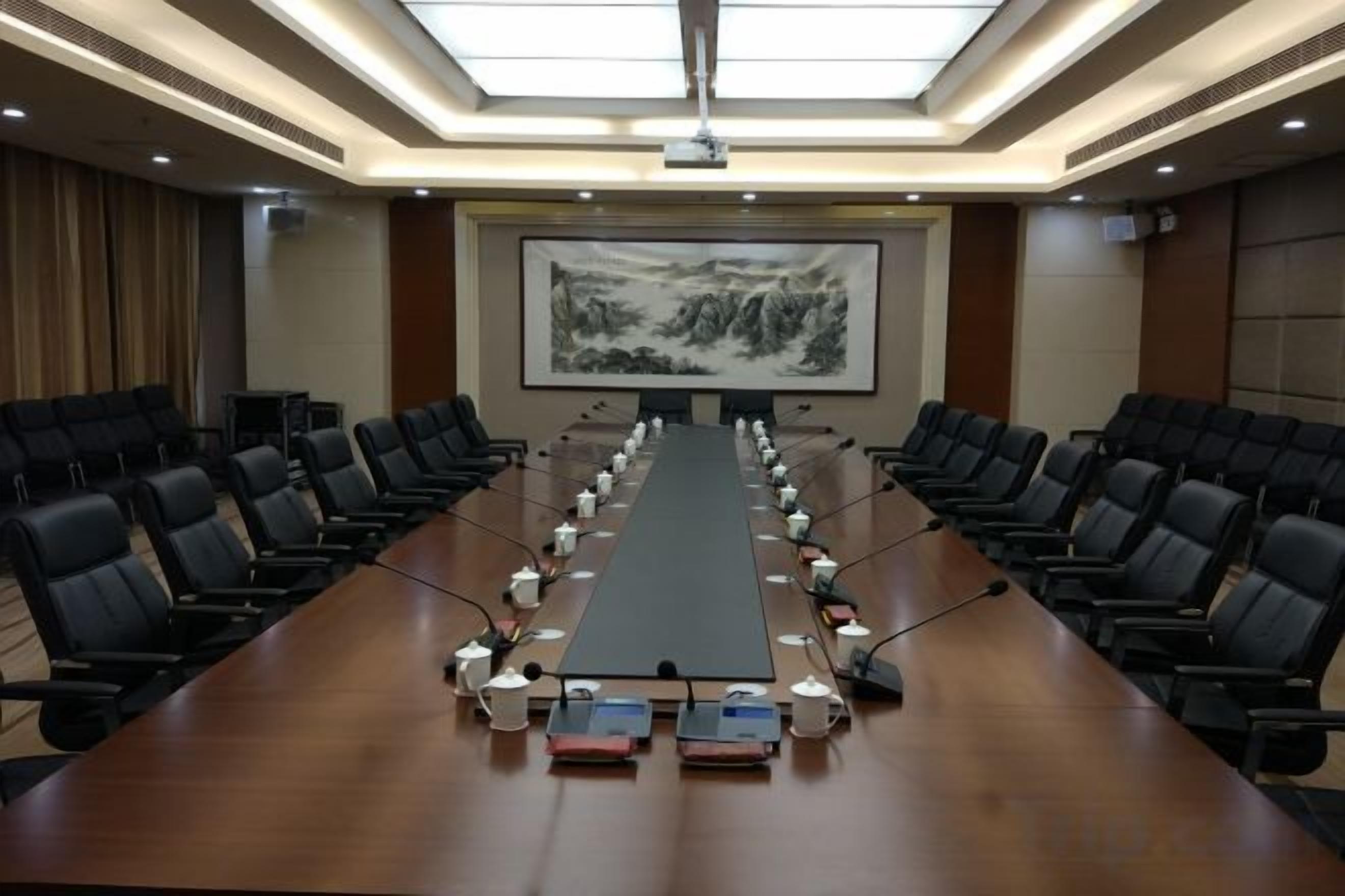 Un salón de conferencias con una larga mesa, sillas y una pantalla para proyector.
