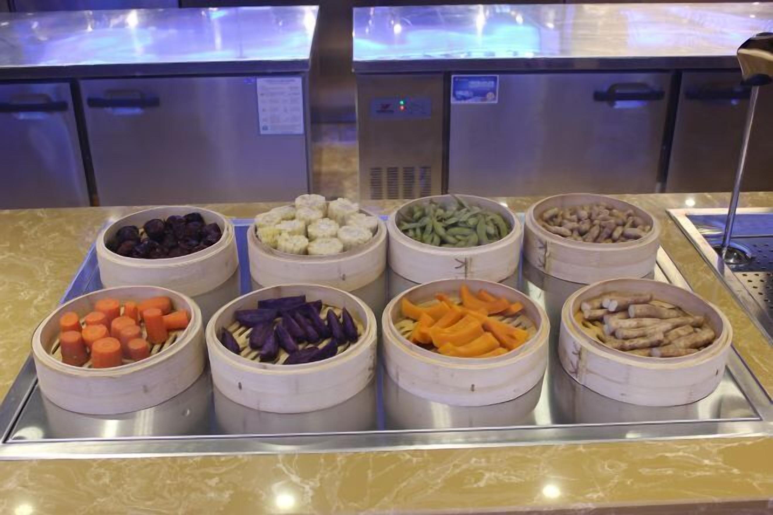 A buffet with various food items in white bowls, including carrots, purple vegetables, green beans, and other mixed vegetables.