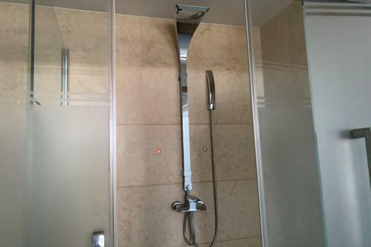 Ducha con cerramiento de vidrio, cabezal de ducha de mano y un cabezal de lluvia fijo.