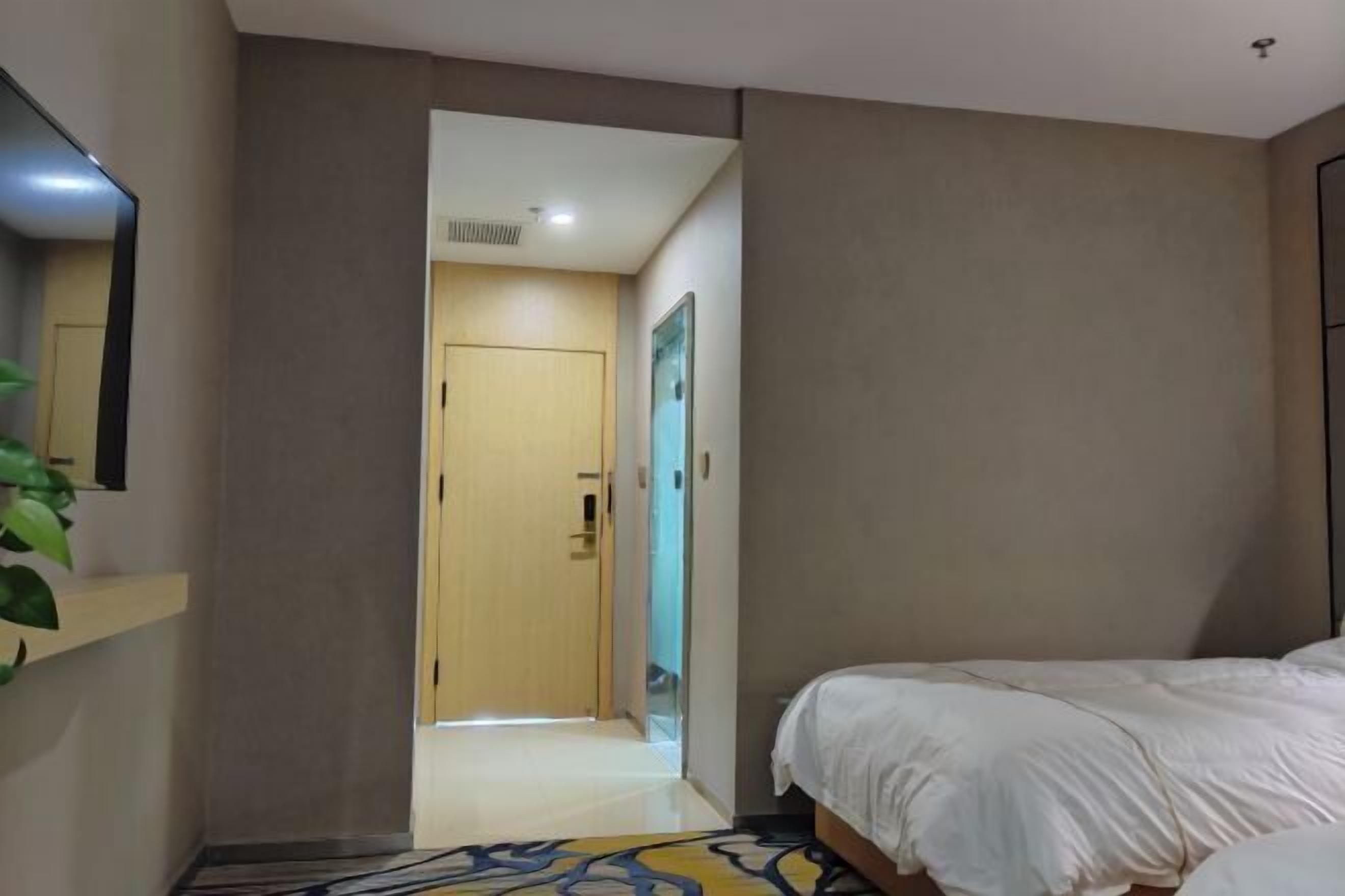 Una habitación de hotel con una cama, un espejo, una puerta y una planta.