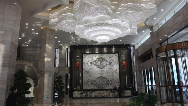 A spacious lobby with a large chandelier, marble wall, and a staircase. - Chiping Hotel (Liaocheng)