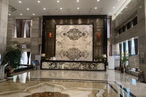 A lobby with a marble reception desk, a large decorative wall, and a patterned floor. - Chiping Hotel (Liaocheng)