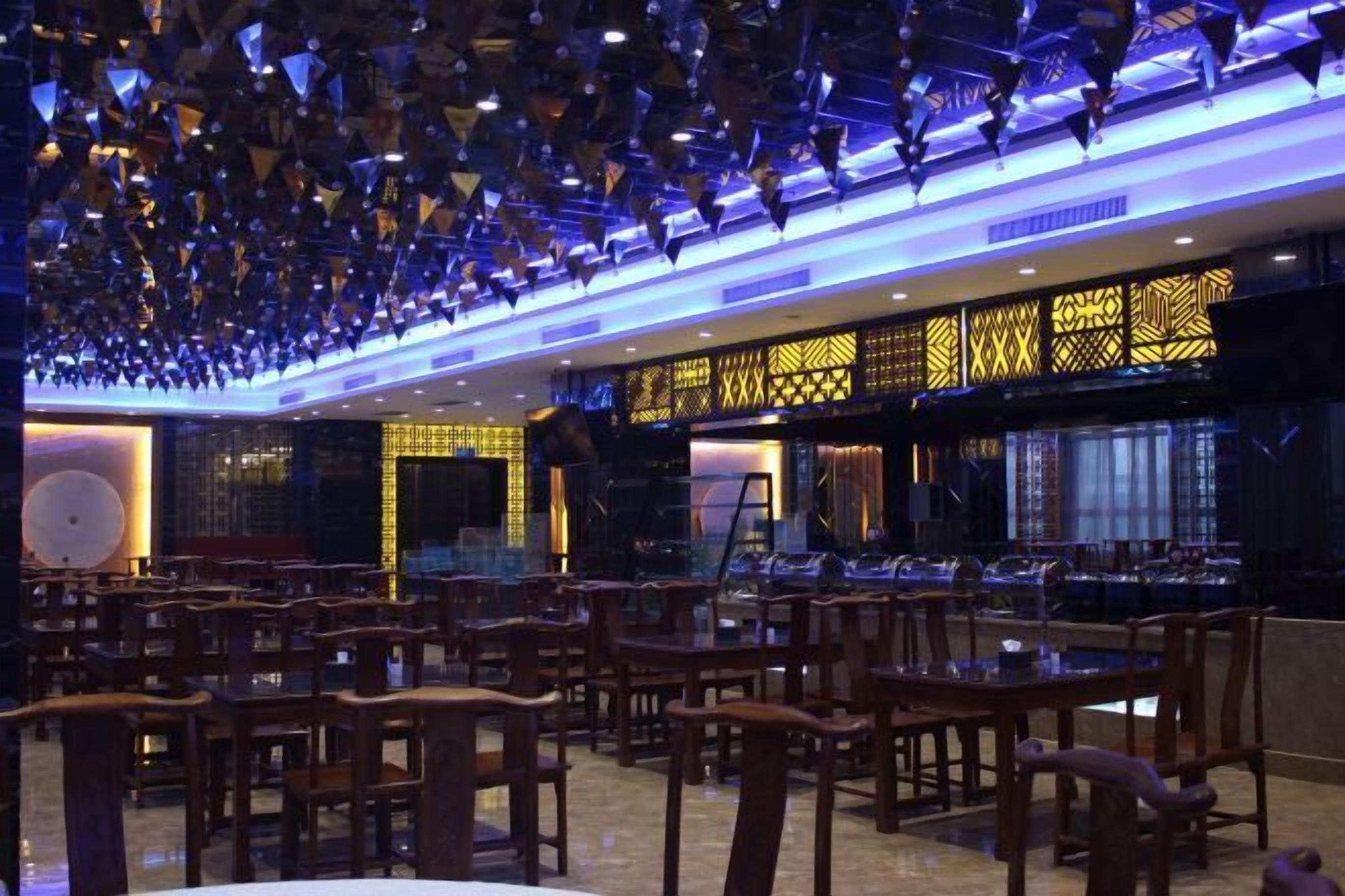 An indoor dining area with wooden tables and chairs, a patterned wall, and a ceiling with hanging lights.