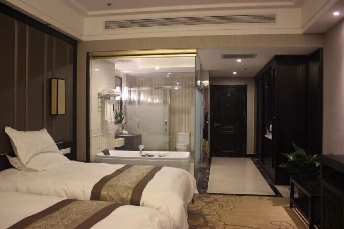 A hotel room with a large bed, a bathroom with a glass shower enclosure, and a dark wooden wardrobe.