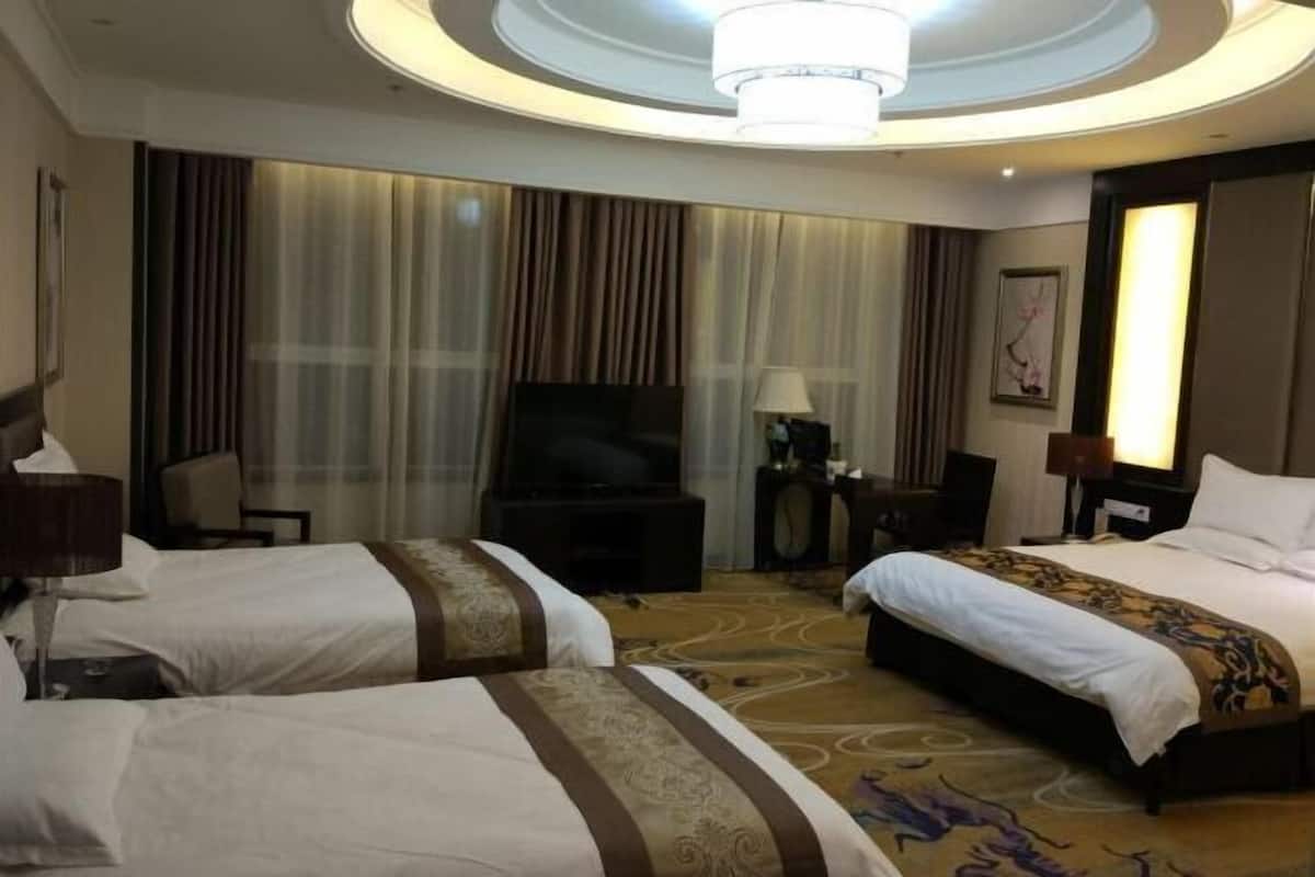 A hotel room with two beds, a TV, a desk, and a chandelier.