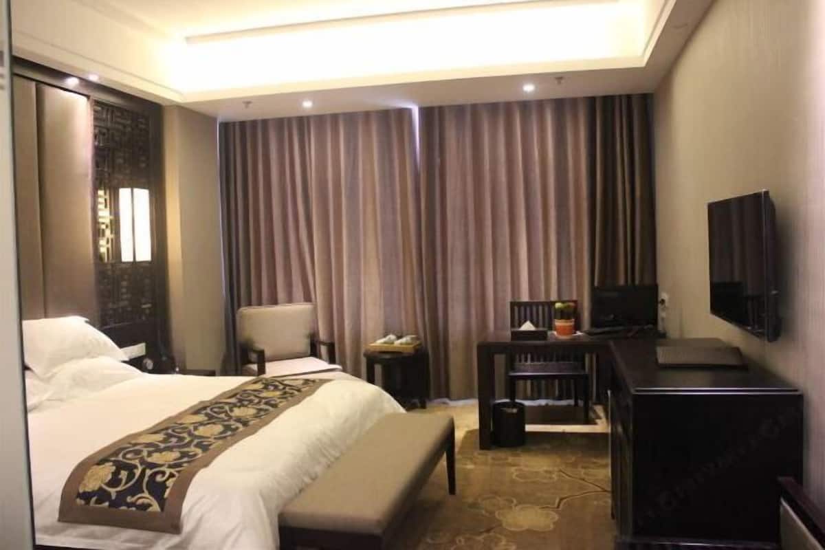 A hotel room with a bed, a desk, a chair, a television, and a large window with curtains.