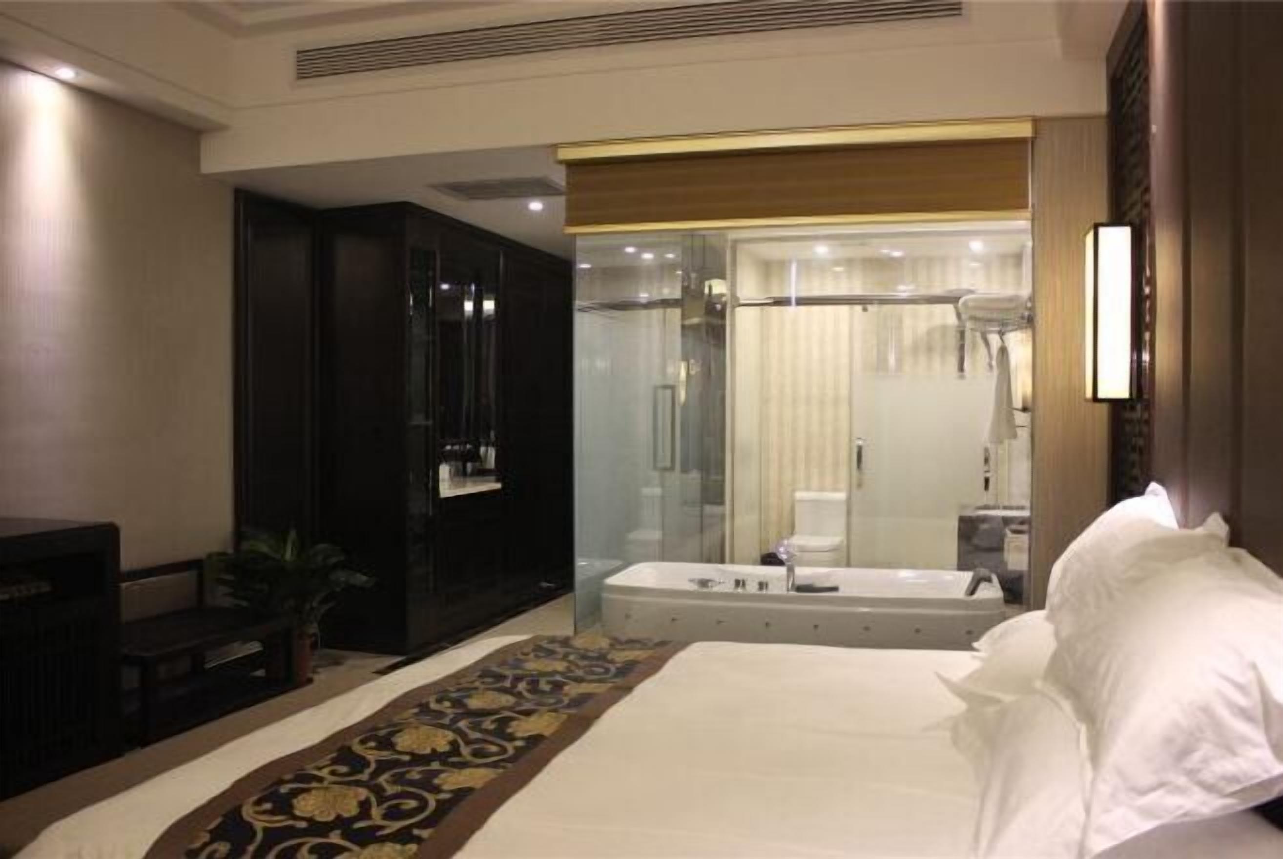 A hotel room with a large bed, a separate bathroom with a bathtub, a desk, and a potted plant.