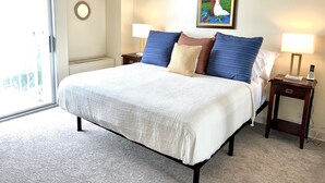 A hotel room with a large bed, two bedside tables with lamps, a painting on the wall, and a view through the glass door.
