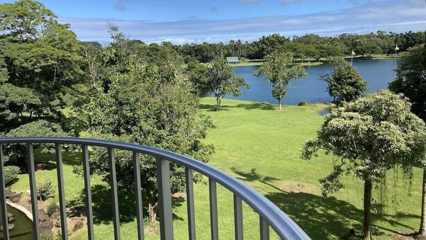 A view from a balcony overlooking a lake with trees and a clear sky.