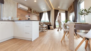 A modern kitchen with white cabinets, a wooden countertop, and a skylight. There is a dining area with a table and chairs, and a view of the outdoors through large windows.