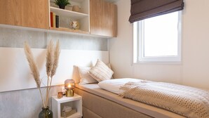 A bedroom with a bed, bedside table, lamp, and a window with a view.