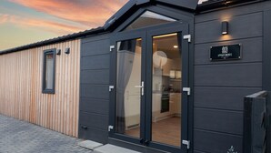 A modern building with a dark exterior, a wooden section on the left, and a glass door entrance.