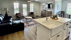 A spacious living area with a black leather sofa, a round coffee table, and a white kitchen island with a sink. - CASITA RETREAT APT: full kitchen, Sleeps 4, near Sand Hollow, Zions, & St George (Hurricane)