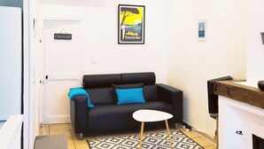 Ein Wohnzimmer mit einer schwarzen Couch, einem kleinen weißen Tisch und einem Teppich mit Muster. An der Wand hängt ein Schild mit der Aufschrift "Côte d'Or Toulon Bay".