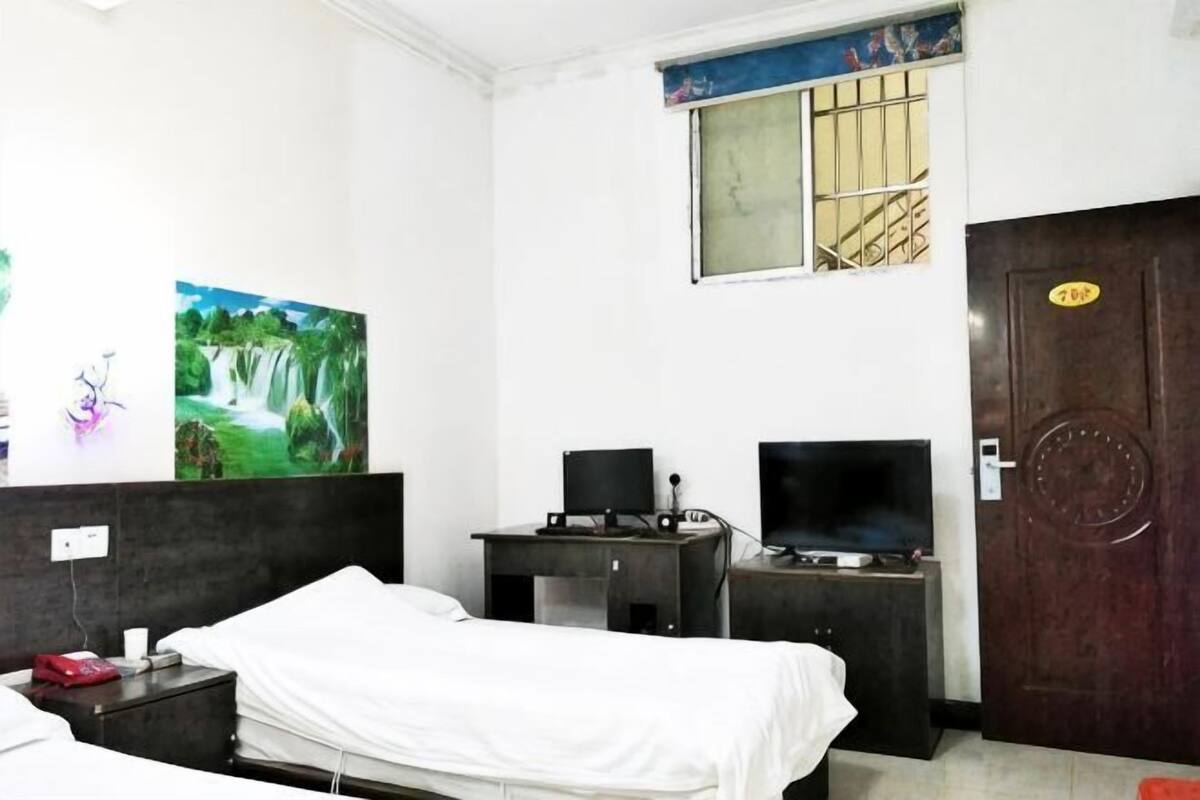 Una habitación de hotel con una cama, un escritorio con computadora, un televisor y una puerta con un número.