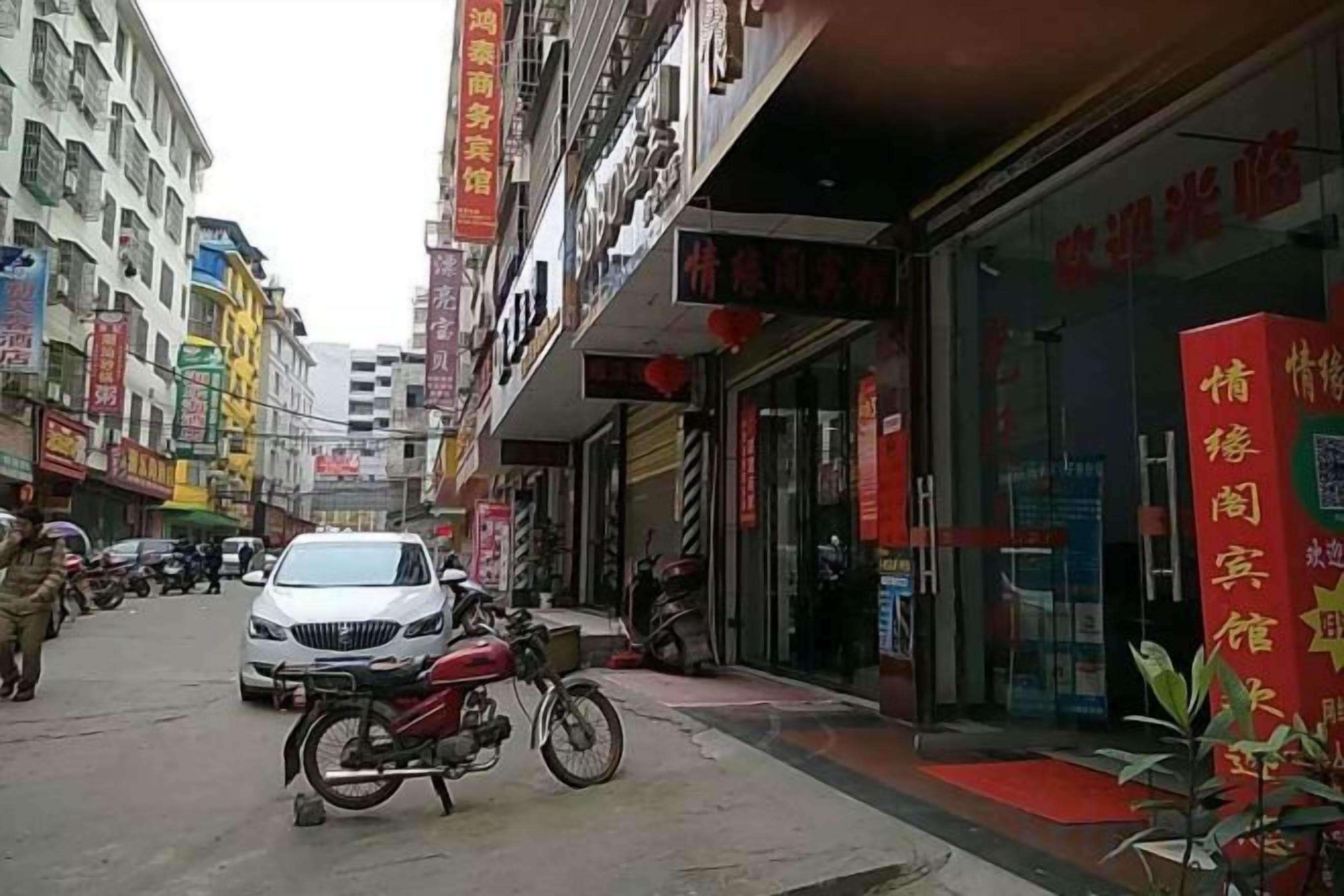 A street with a motorcycle parked in front of a building with a red awning and a glass entrance.