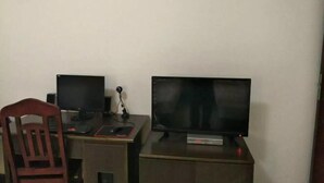 Une pièce comprenant deux bureaux, chacun équipé d’un écran d’ordinateur et d’un clavier, d’une chaise et d’un téléviseur posé sur un meuble.