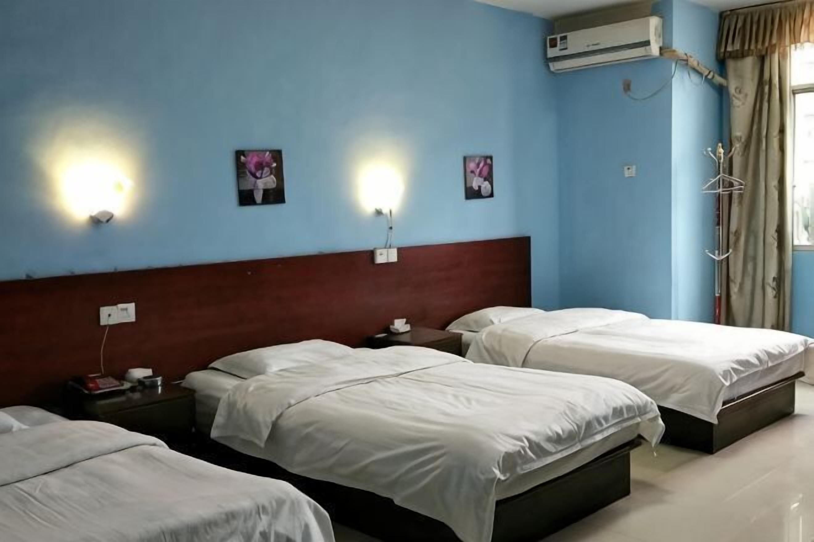 Ein Hotelzimmer mit drei Betten, einem Holz-Kopfteil, Wandleuchten und einer Klimaanlage.