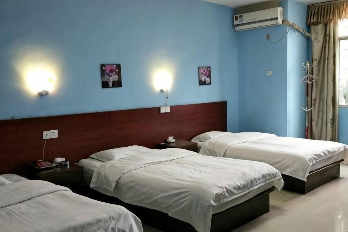 Habitación de hotel con tres camas, cabecera de madera, luces fijadas a la pared y un equipo de aire acondicionado.
