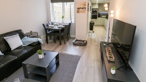 A modern living room with a black leather sofa, a dining table with chairs, a coffee table, and a TV stand with a flat-screen TV. - North Bay Retreat (Scarborough)
