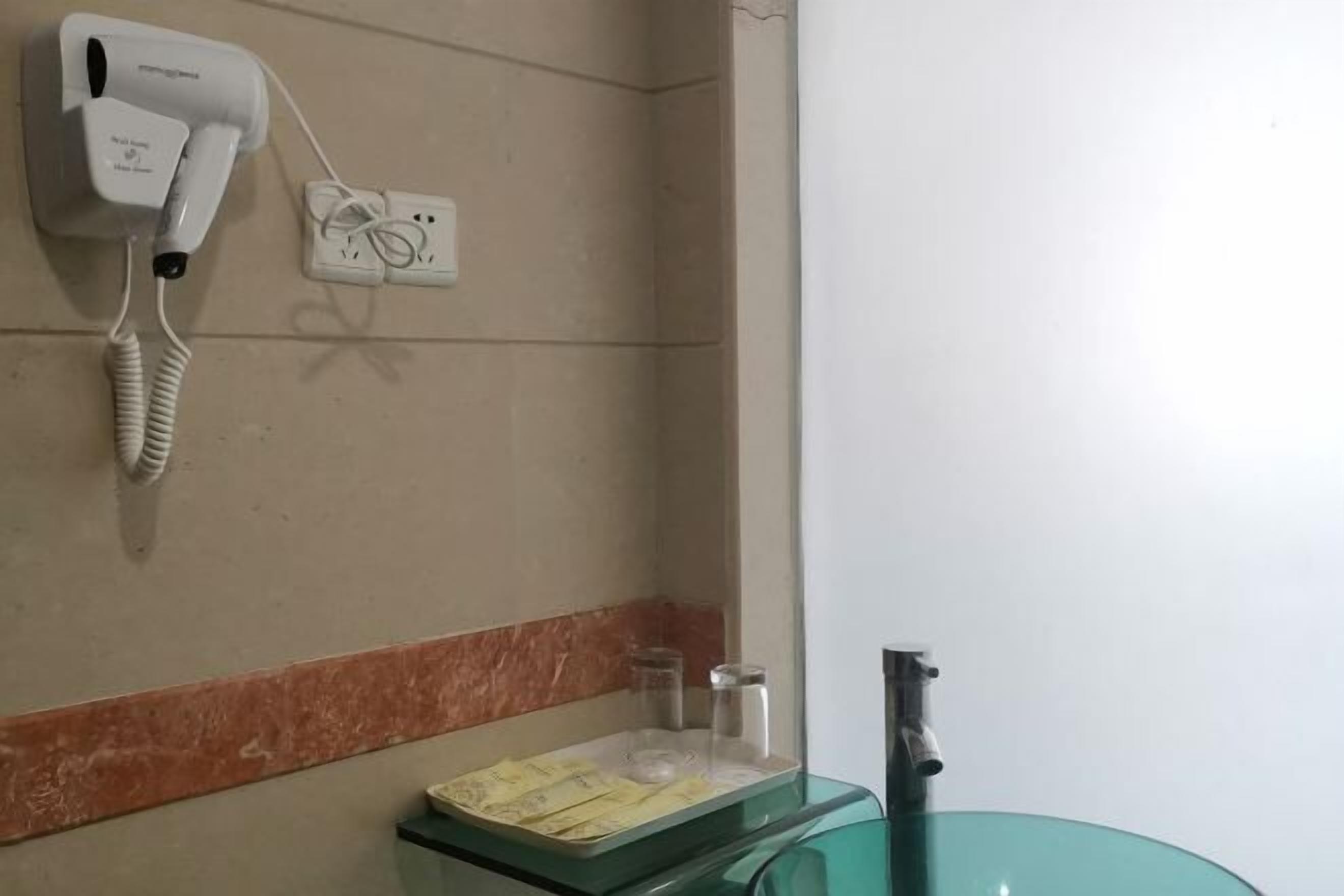 Casa de banho com secador de cabelo, lavatório de vidro e espelho.